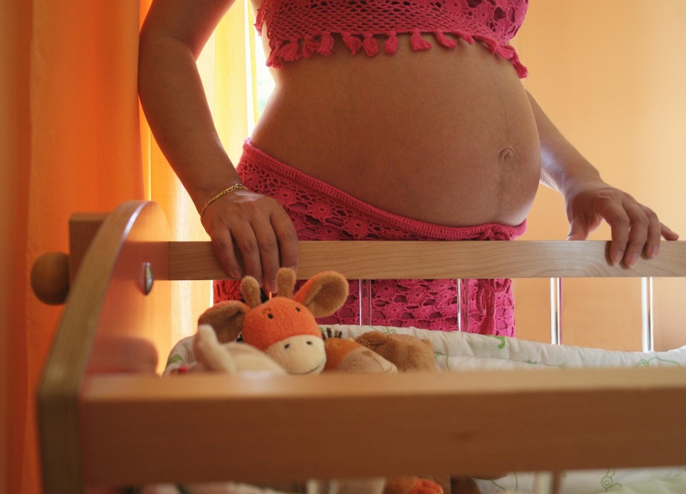 Bauch einer schwangeren Frau mit Kinderbett im Vordergrund