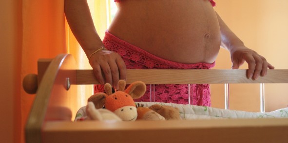 Bauch einer schwangeren Frau mit Kinderbett im Vordergrund